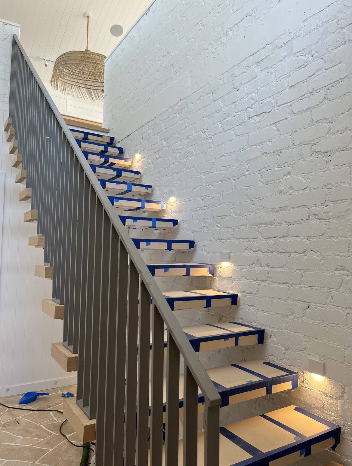 Floating timber staircase against white brick, with LED step lights set into the wall