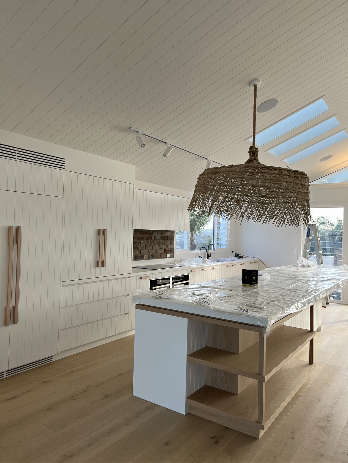 White kitchen with a marble island, a woven pendant light and track lighting under skylights