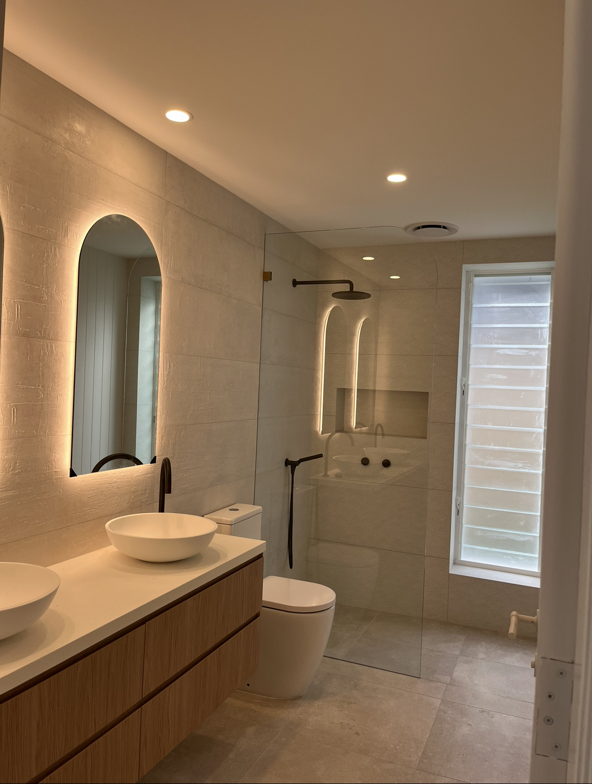 Bathroom with backlit arched mirrors, downlights and black tapware
